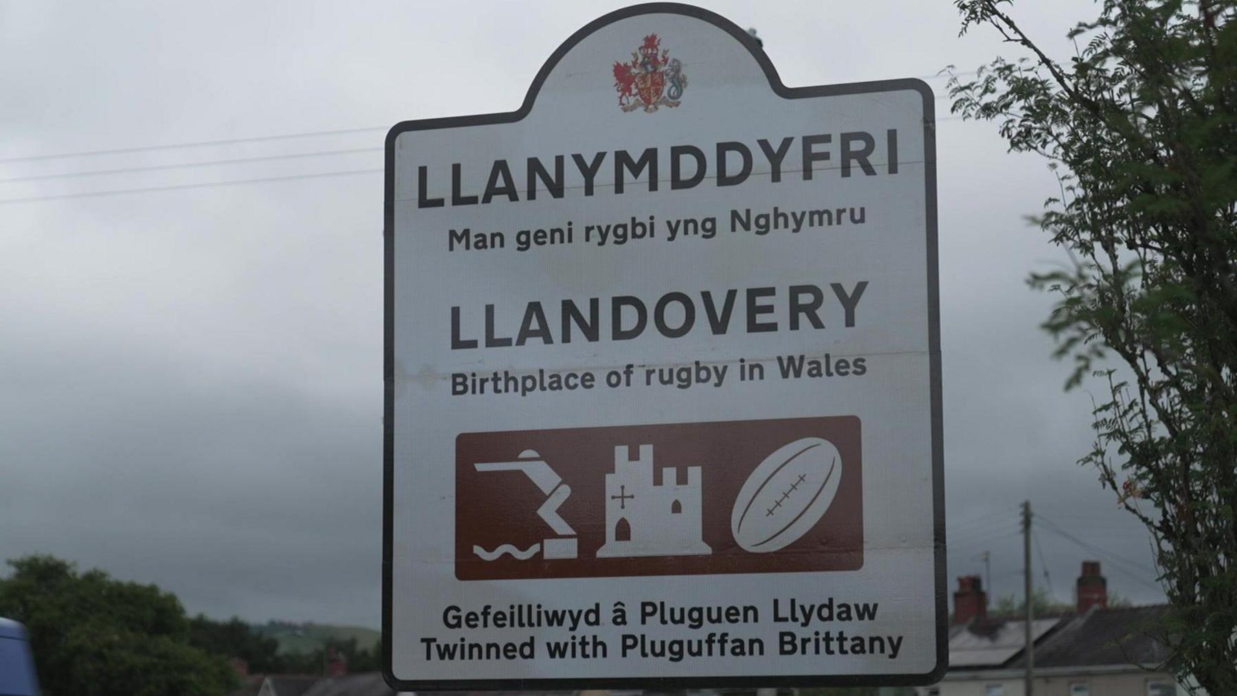 A white road sign in Llandovery with the town's name written in Welsh and English. The sign also has 'The birthplace of rugby in Wales' written on it.