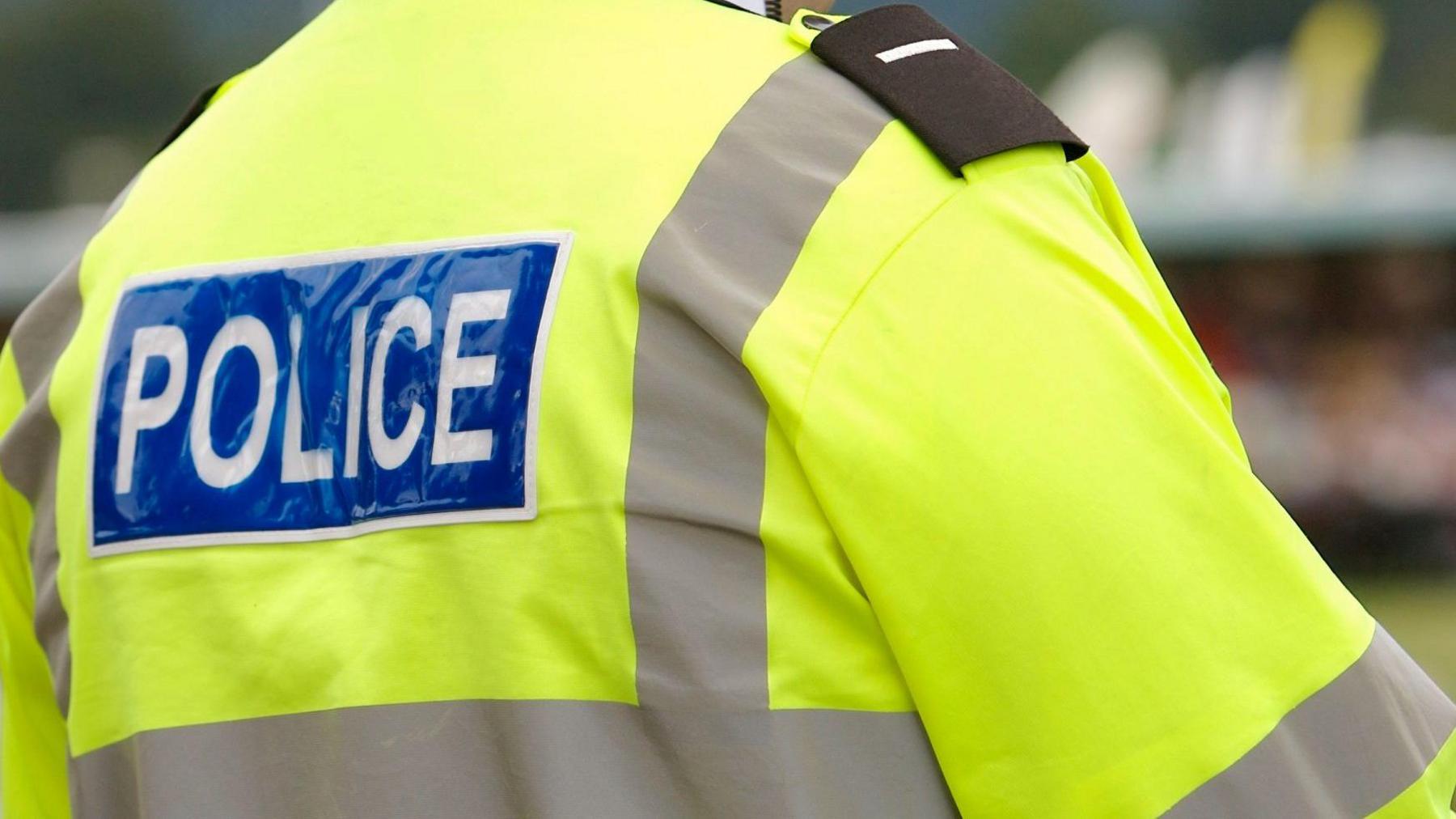 A police officer in a high-vis jacket stands facing away from the camera