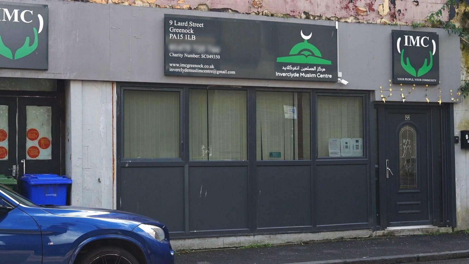 The street entrance to the mosque which has four windows and a door, with three signs saying IMC above them