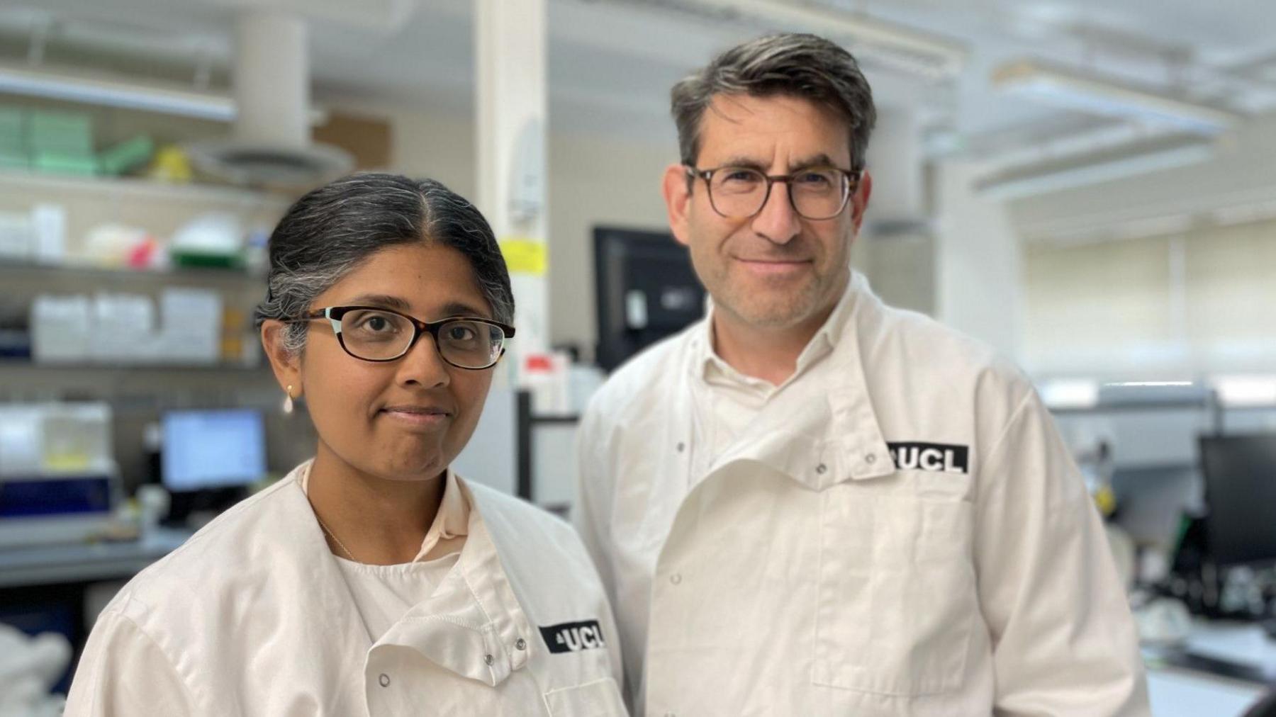 Dr Ashvini Keshavan and Prof Jonathan Schott, dressed in white lab coats, stand side by side in their laboratory