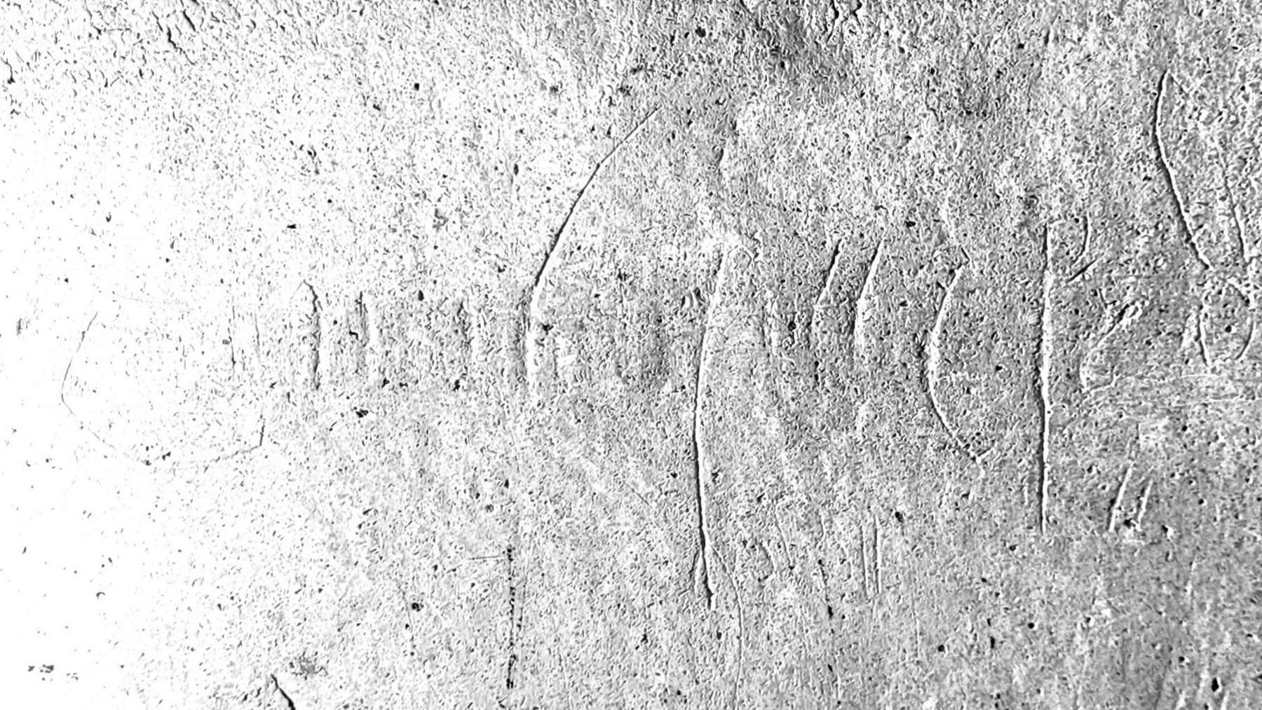 A carving etched into a stone wall. The name Hickman is inscribed. It is upside down