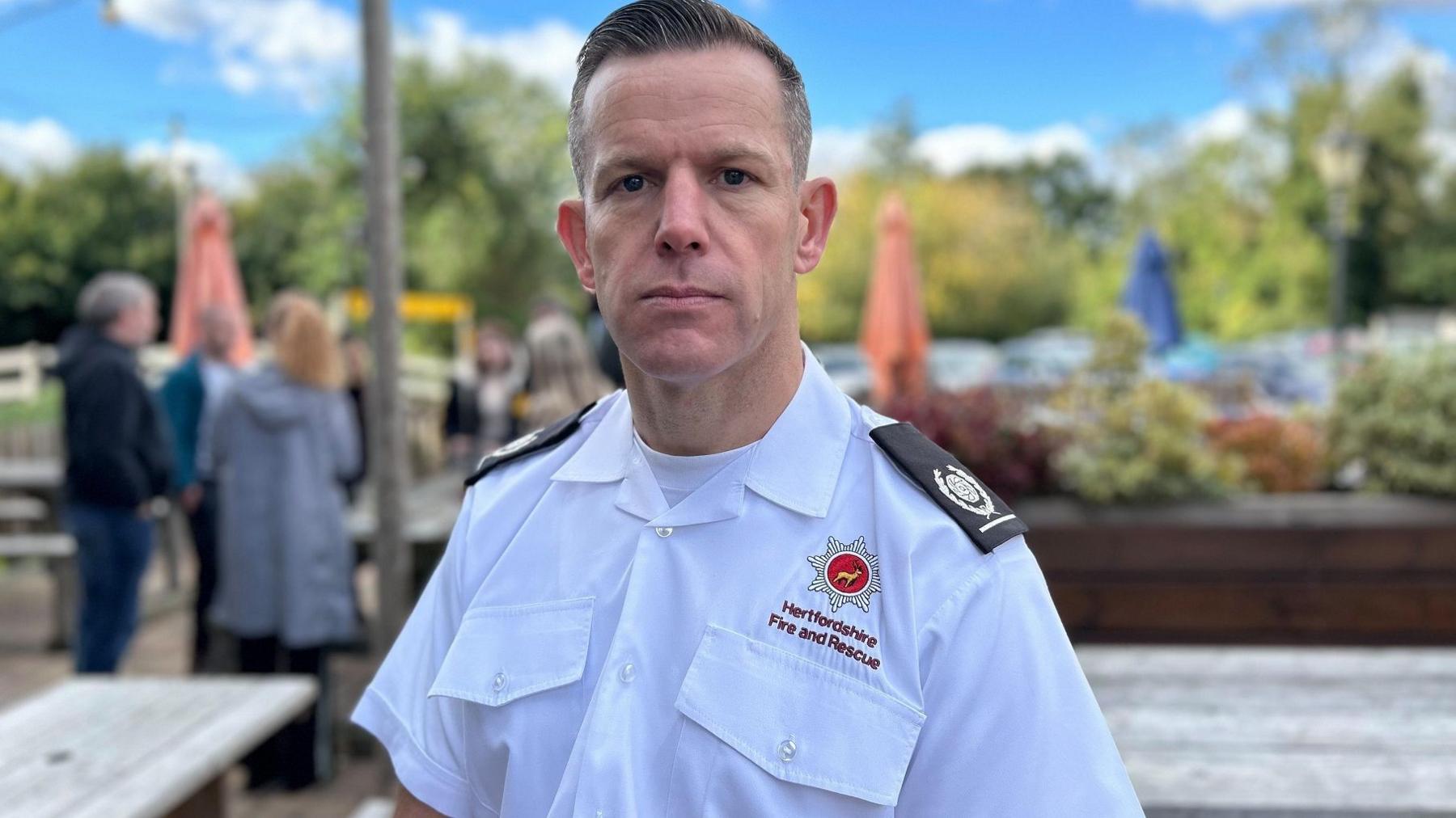 Wayne Gibbons, wearing a fire service white short-sleeved shirt, stands in a pub garden