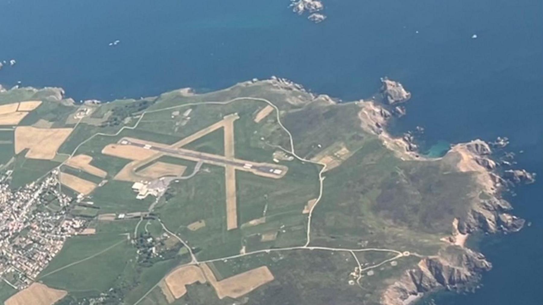 An aerial view of Alderney's runway. There are three landing strips in the shape of an A on a grassy island with steep cliffs.