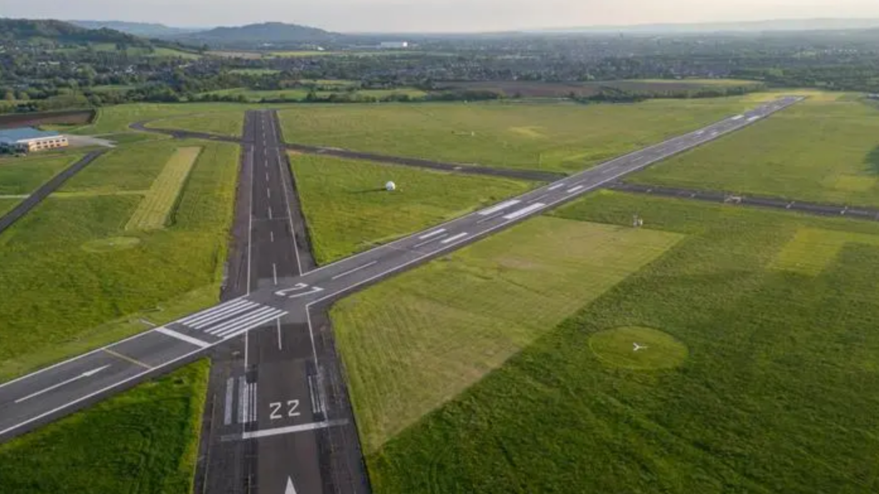 A drone shot of Gloucestershire Airport's runways. Green fields can be seen in the background.