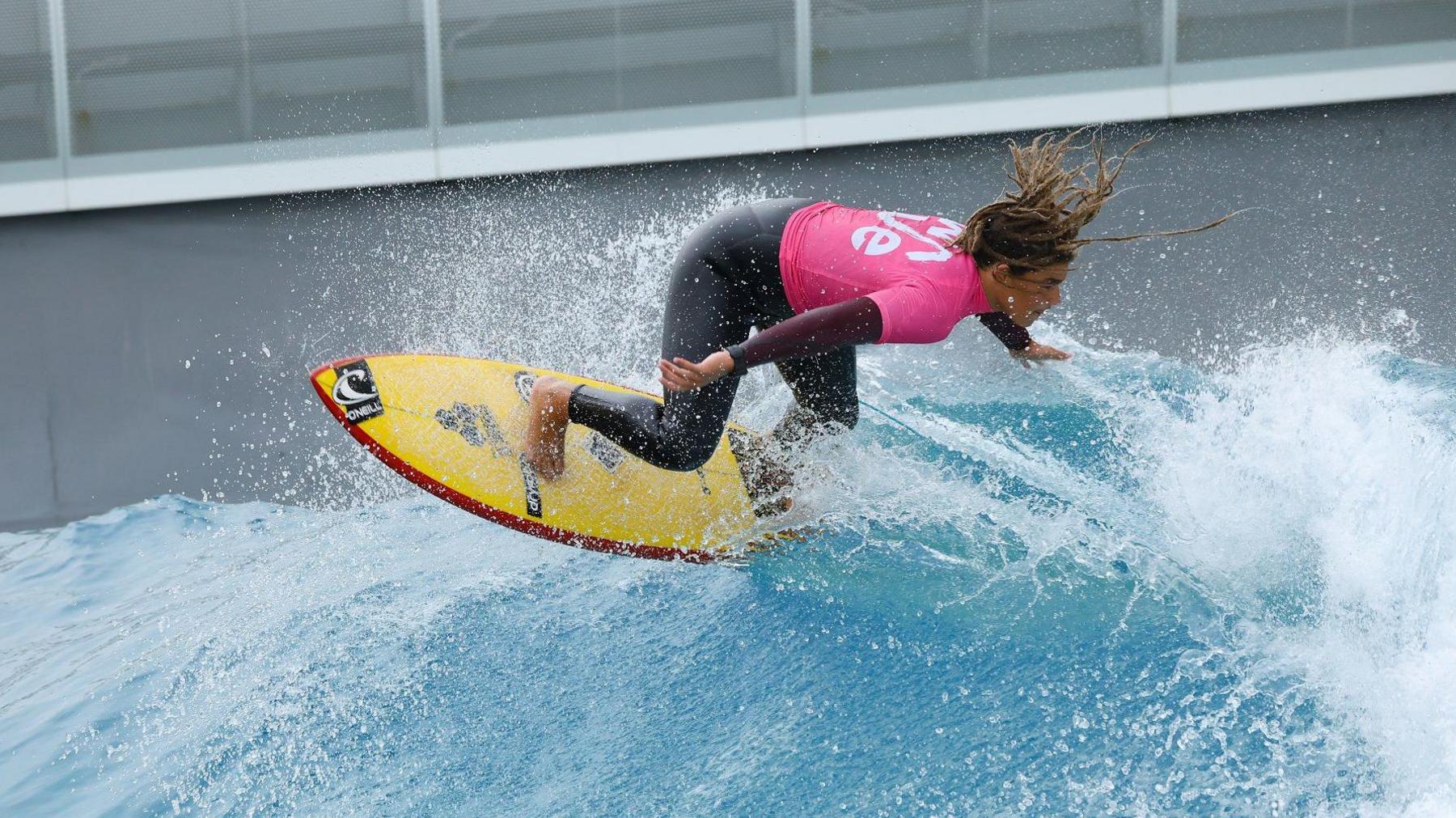 A young surfer in a pink top rides a wave at The Wave surfing attraction near Bristol