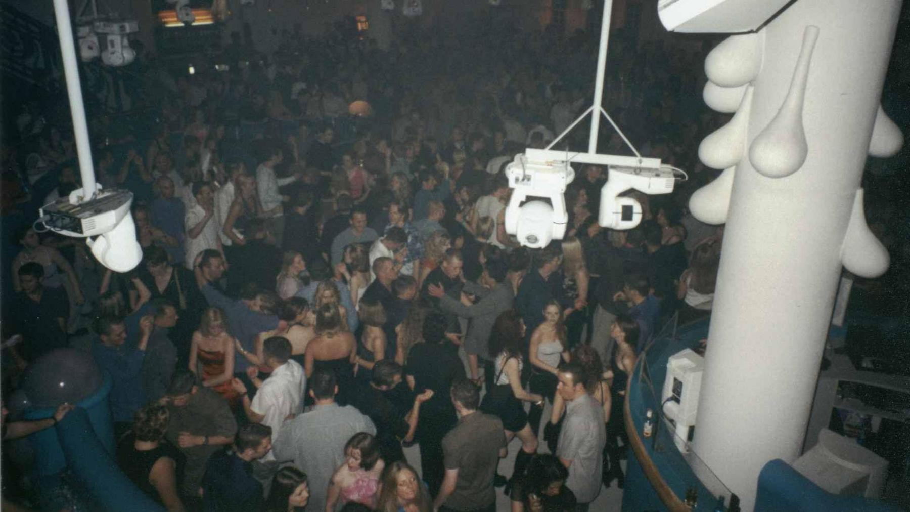A crowd of people dancing in a nightclub flanked by lights.