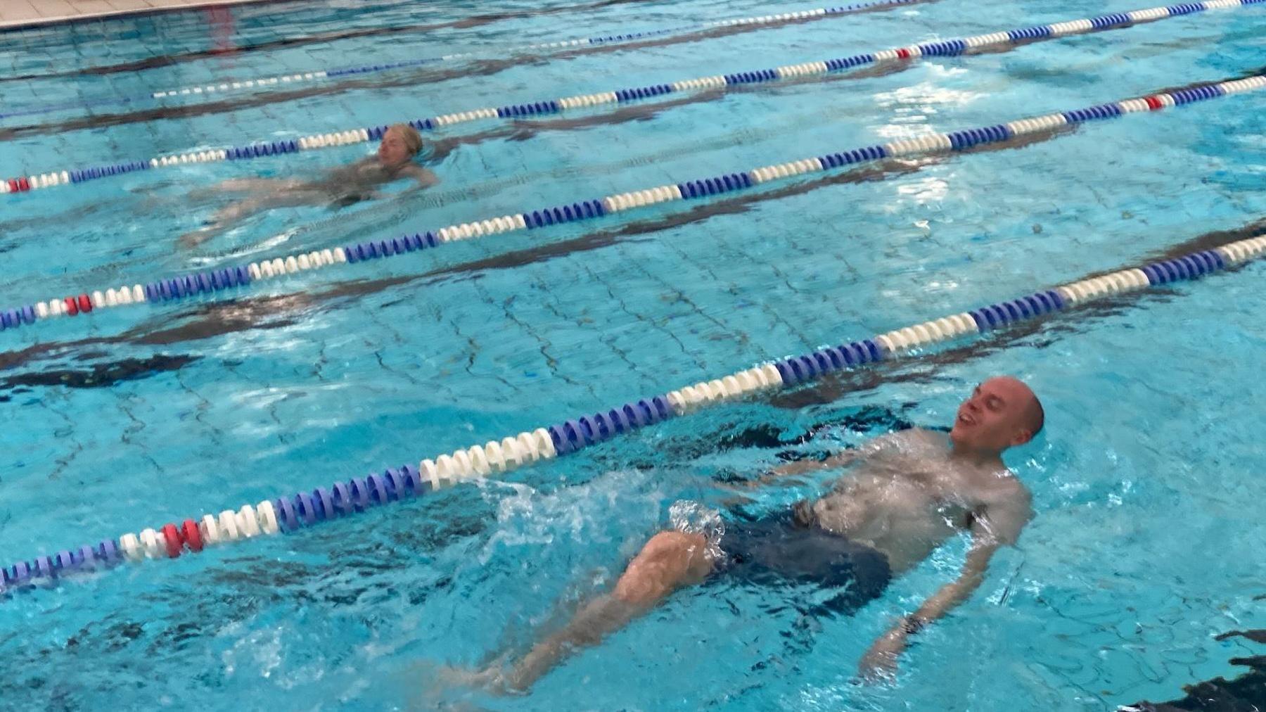 Sophie Law and Dan Freeman swim backstroke in the pool in their own separate lanes.