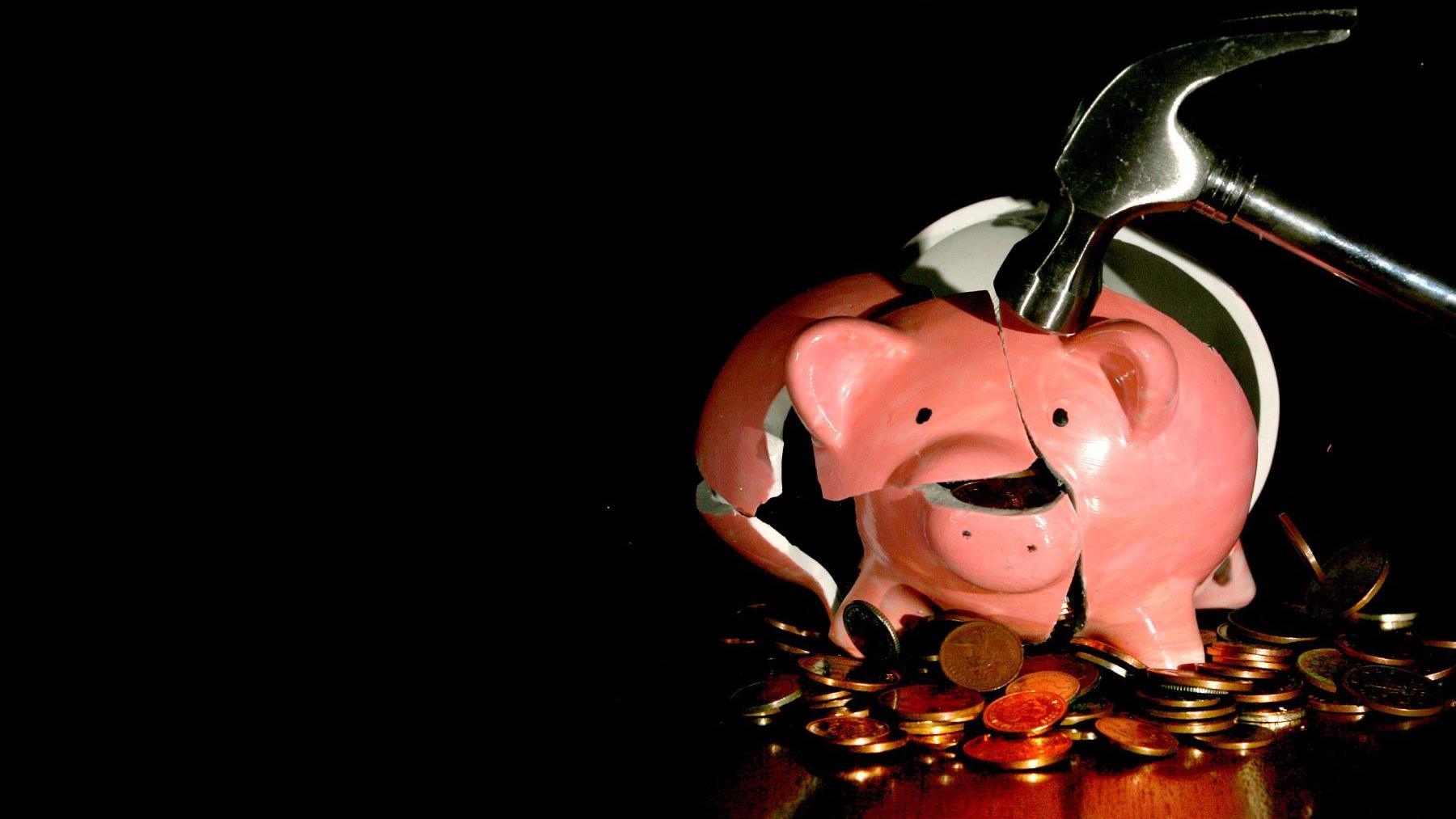 A piggy bank being broken by a hammer as money falls out.