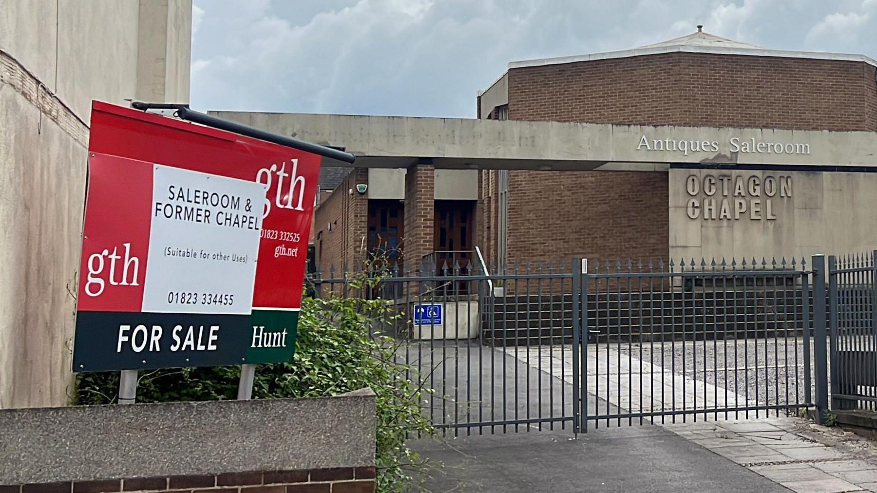 a for sale sign outside the Octagon Chapel with the building in the background behind gates