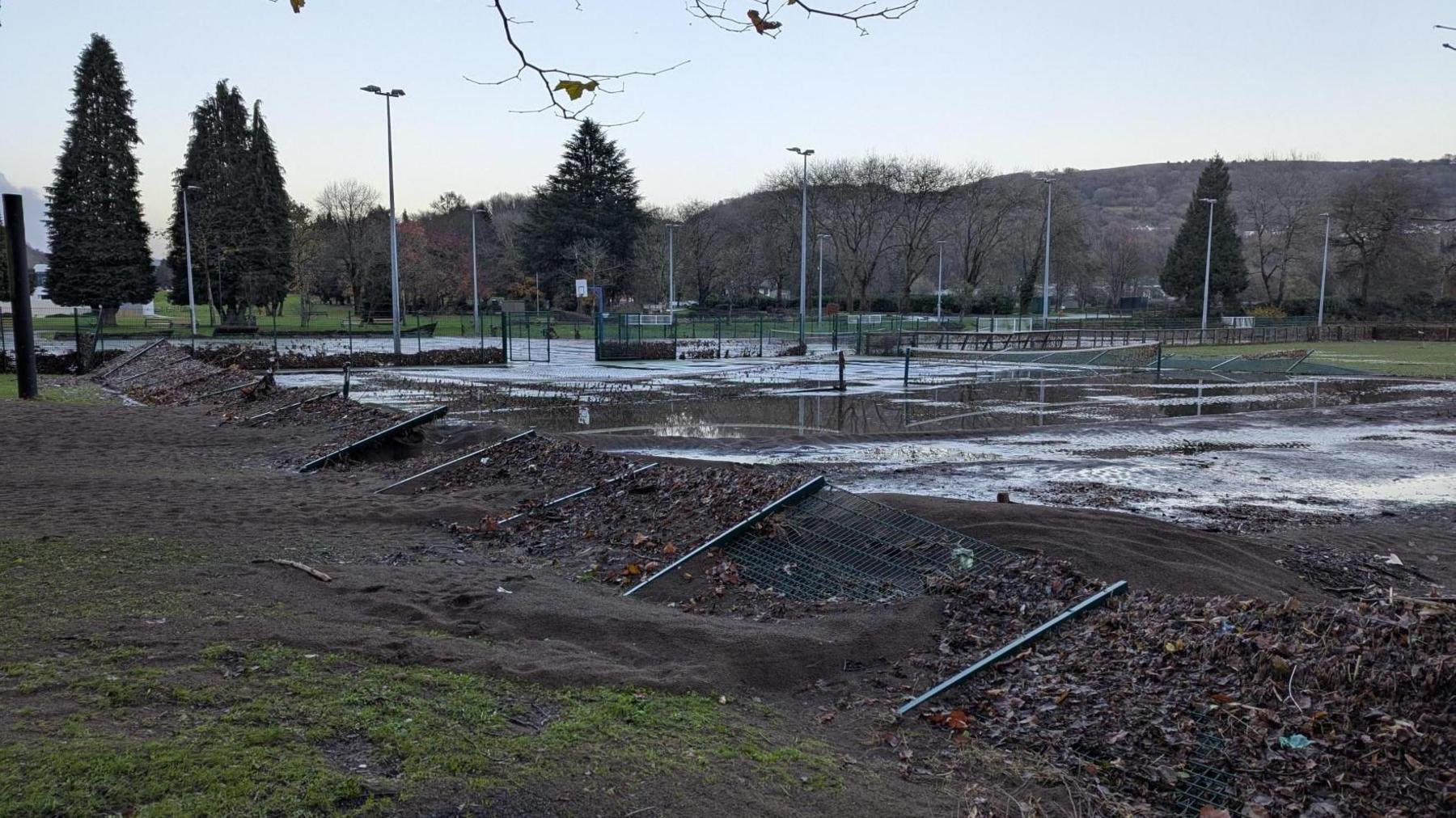 Railings of the sports court are flattened, and the tennis courts are almost swamp-like, covered in thick, dark silt at Pontypridd Lido