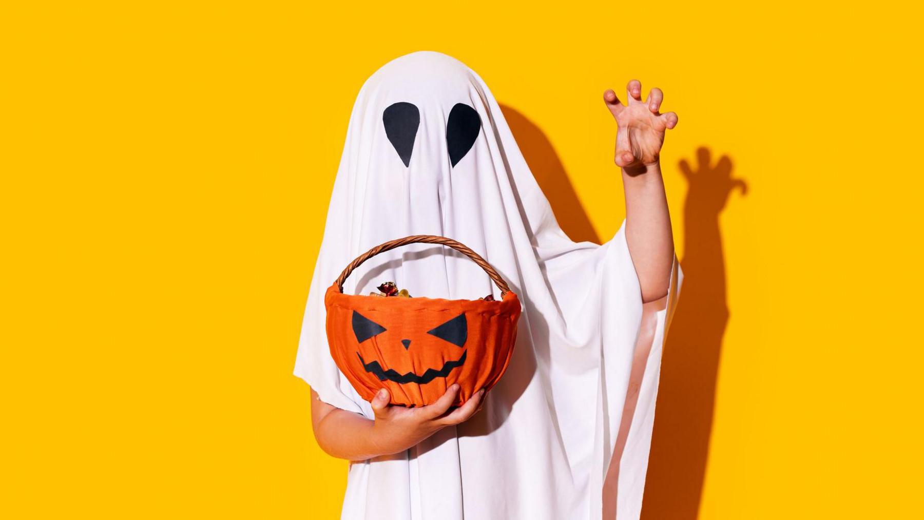 child dressed as ghost holding a pumpkin basket. 