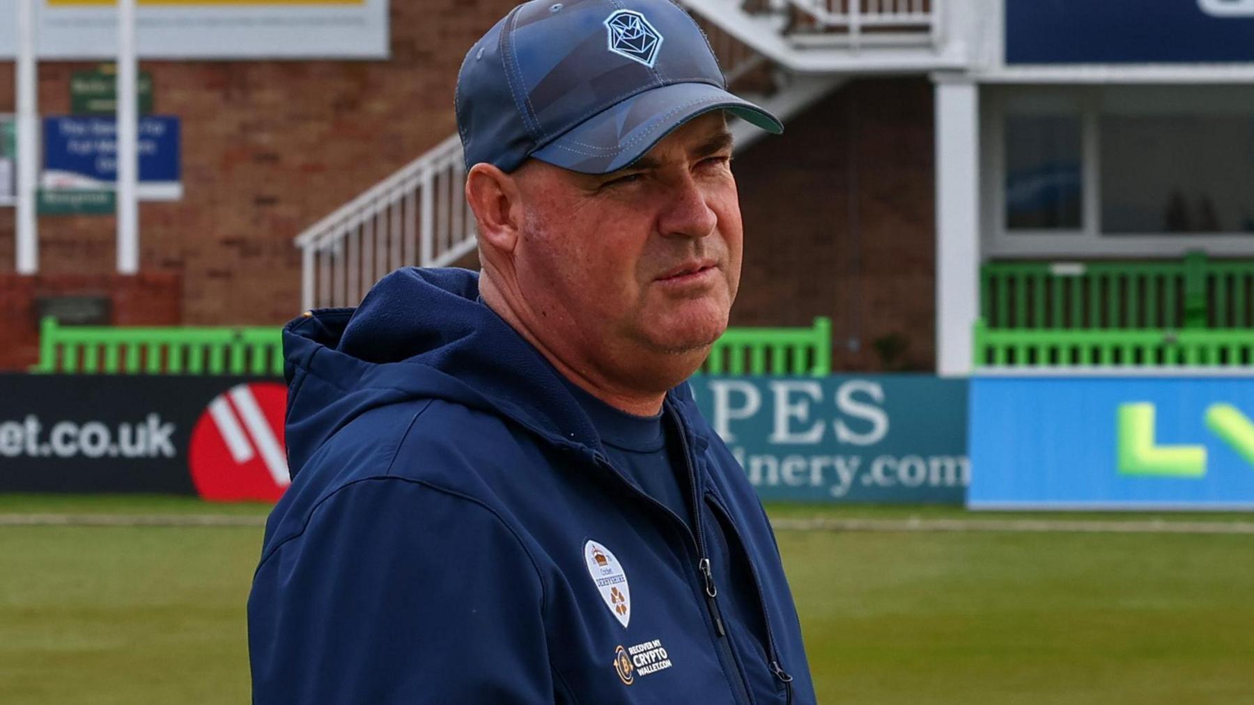 Mickey Arthur stands on the pitch with his phone out before Derbyshire's match against Leicestershire