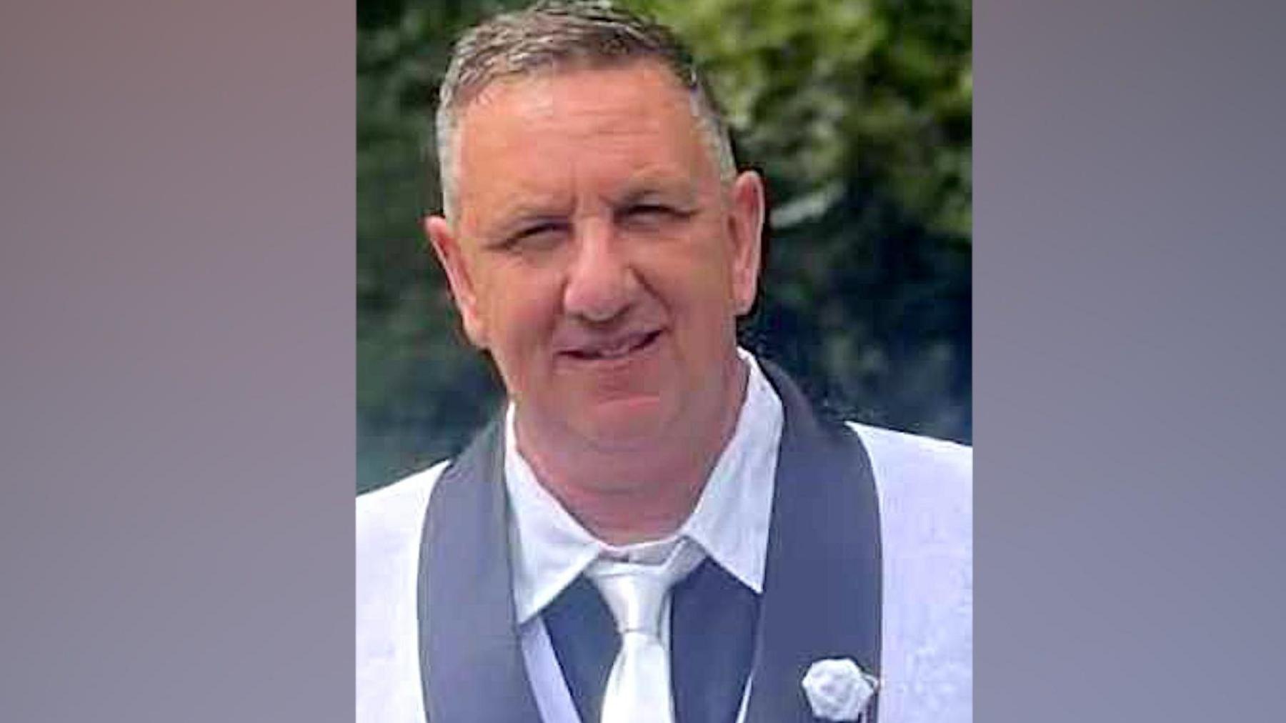 Man in a grey suit and white shirt posing for a picture. He is clean shaven, with short receding grey hair.