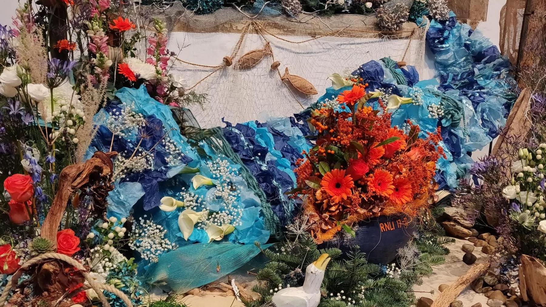 Two fish figures in a net are surrounded by what appears to be blue crepe paper and red flowers.