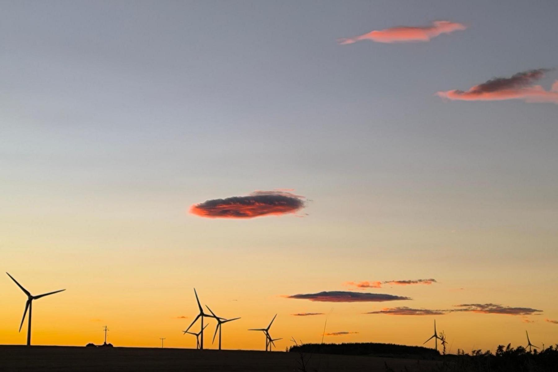 Clouds glowing red and pink above a wind farm. The sky along the horizon is a dark yellow.