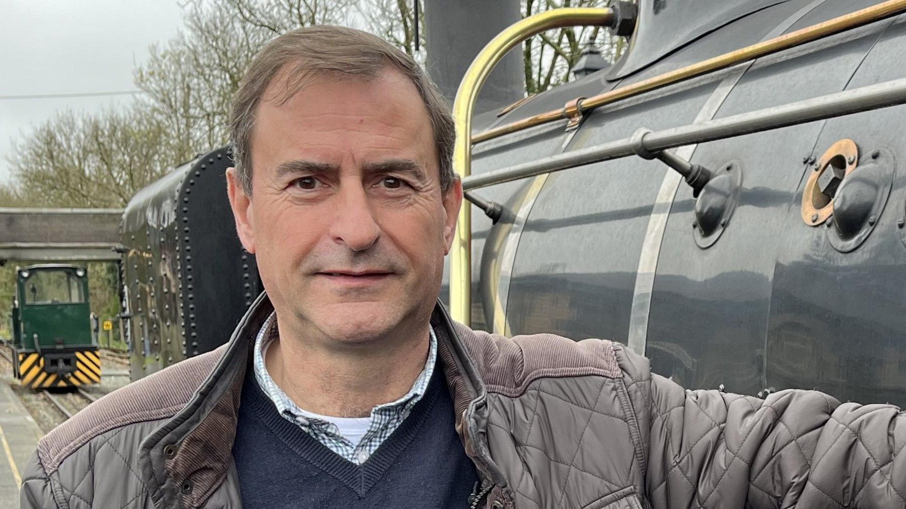 Welsh Highland Railway's boss Paul Lewin stands next to train in a brown jacket