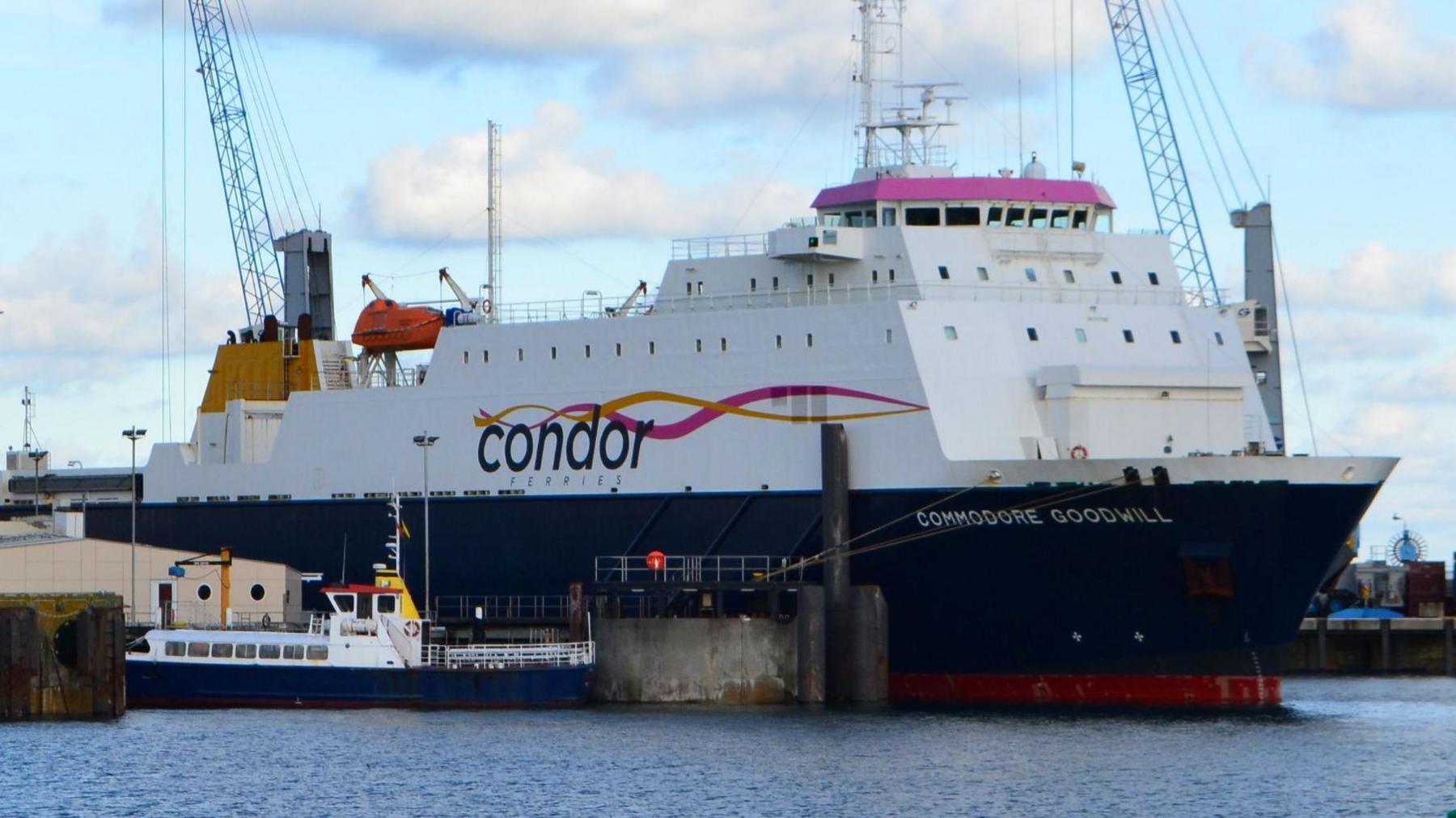 A wide shot of Commodore Goodwill entering a harbour. It is big a white, with a navy blue underside.