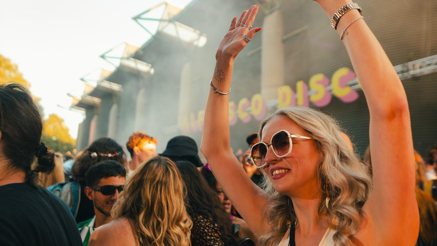 A woman wearing a white top and sunglasses waves her arms during an Alfresco Disco event in Bristol