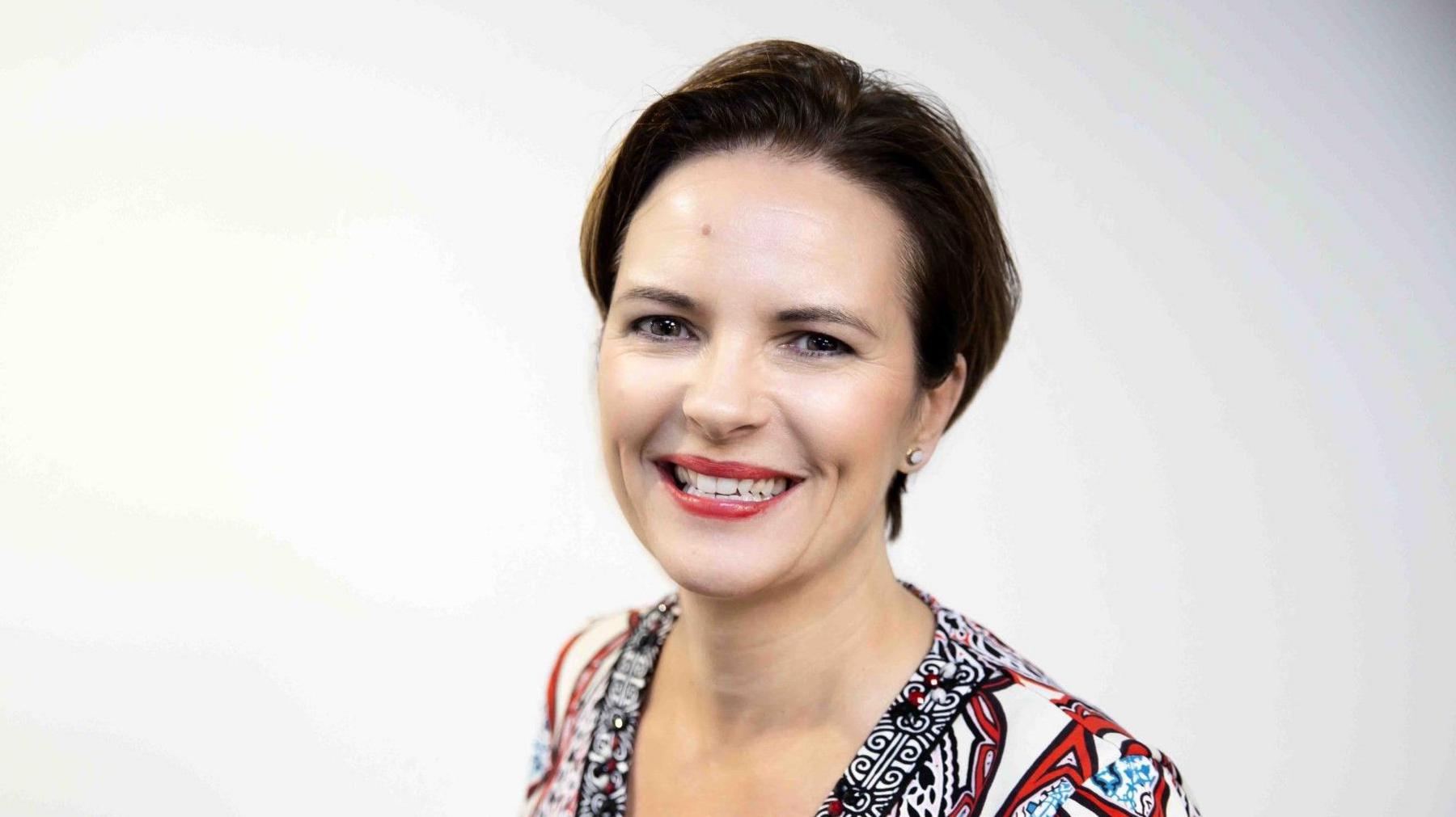 Kerry Reynolds with short dark hair, smiling at the camera and wearing a black, red, blue and white patterned top