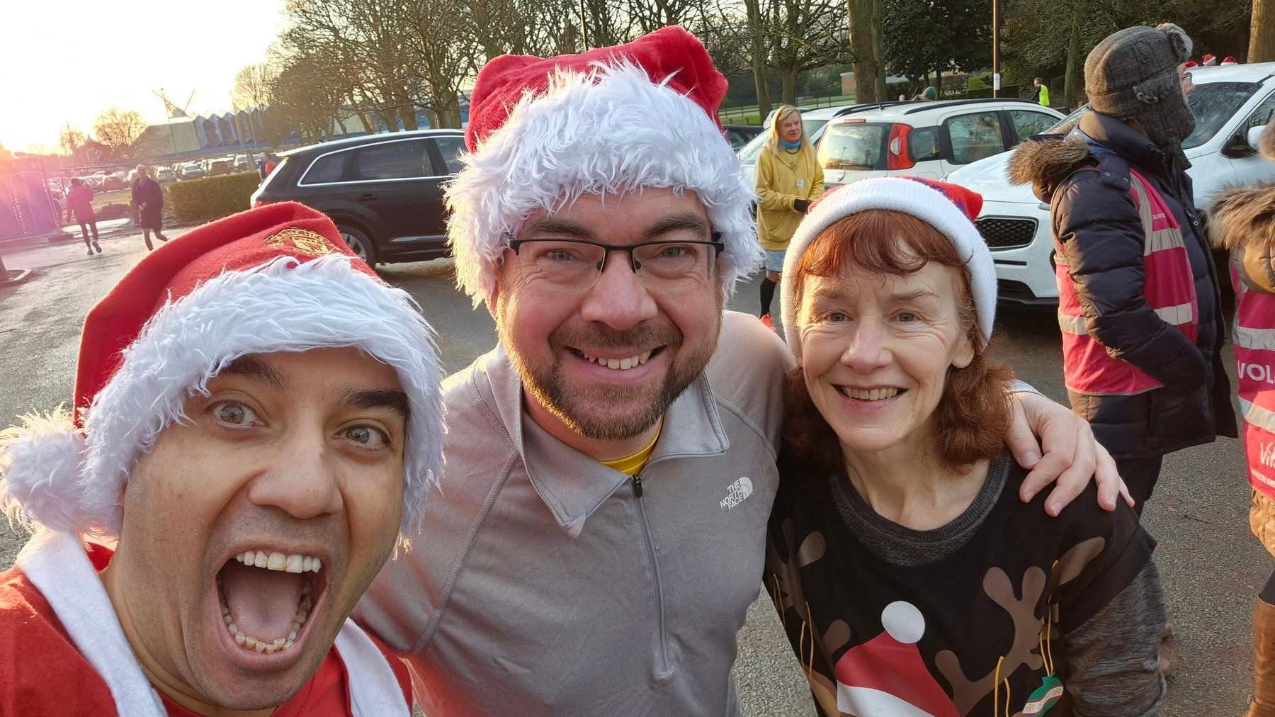 Three people wearing Santa hats smiling at the camera. 