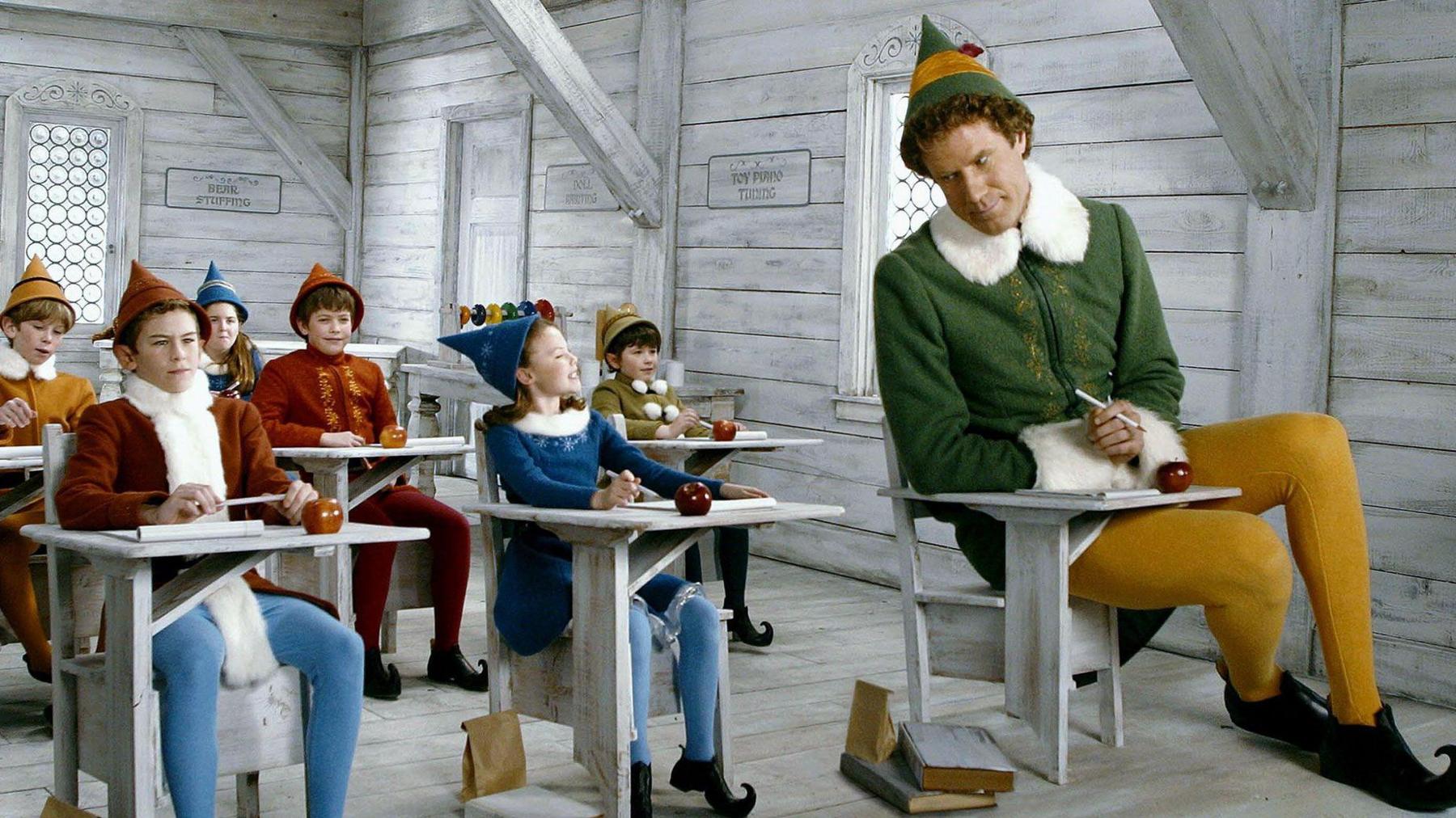 A still from the Elf movie where Will Ferrell is wearing his green and gold elf costume while sat in a school full of children playing other elves.