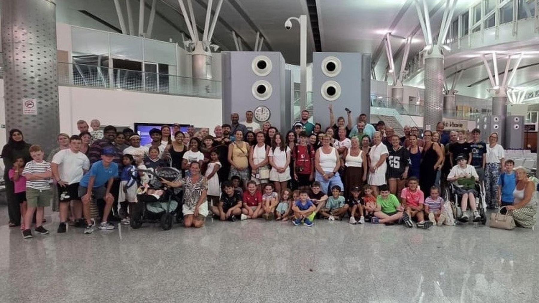 A large group of people standing in an airport. There are people of all ages.
