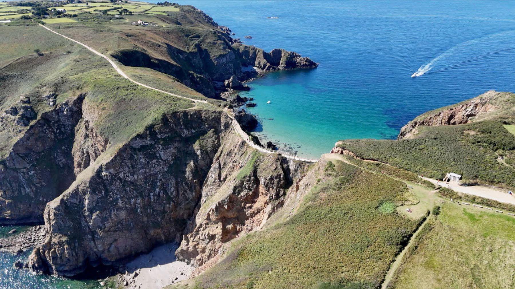 An aerial view of a narrow strip of land joining a peninsula to a small islands. A small road