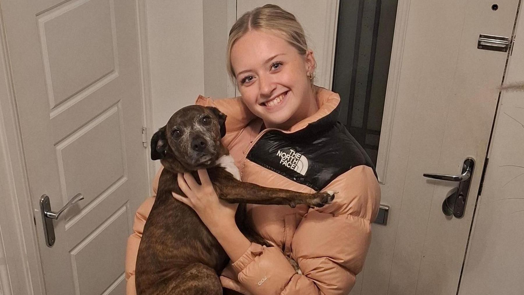 Menyw ifanc yn gafael mewn ci o flaen drws