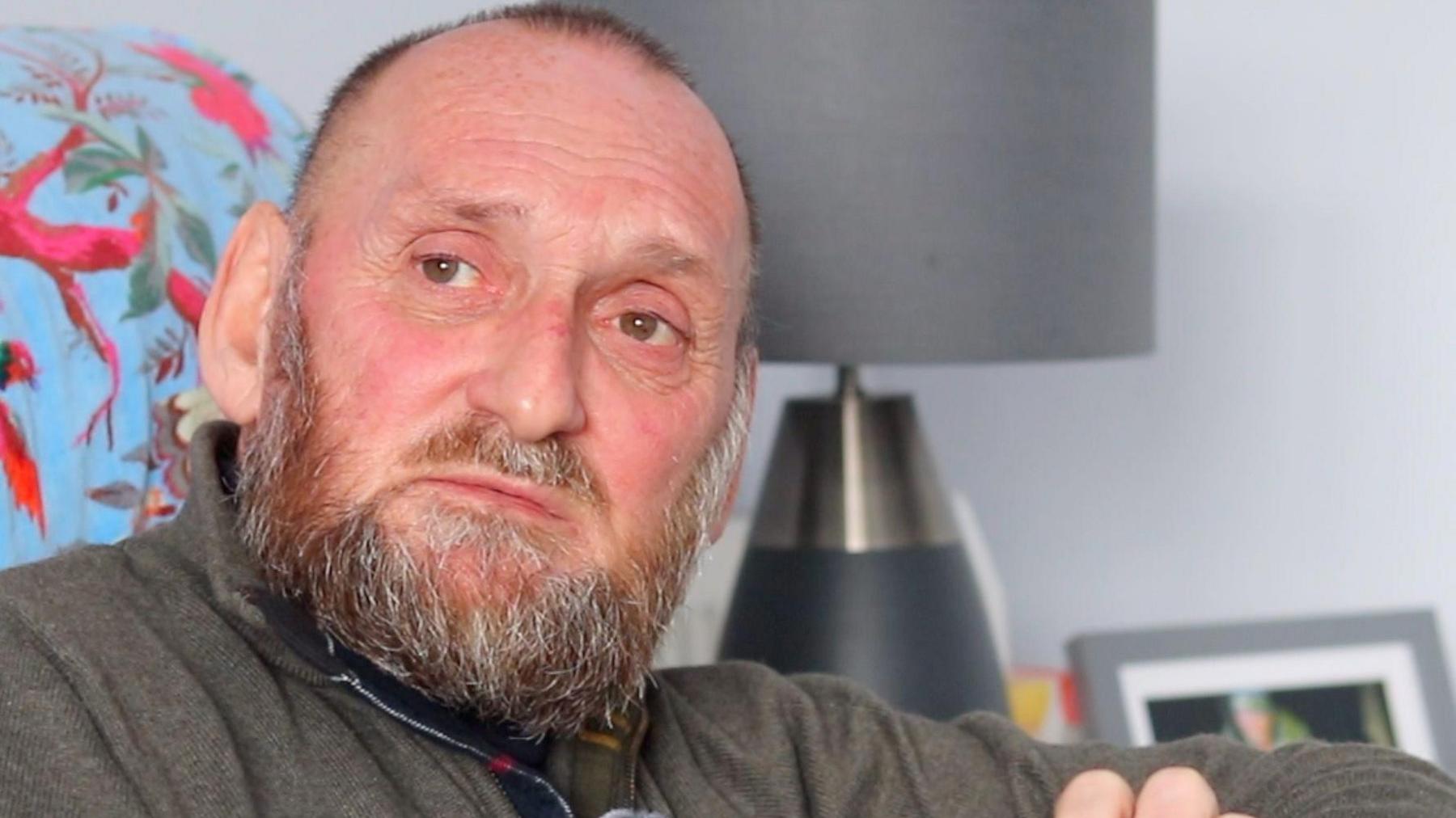 Phil Stevens - a white, bearded man staring towards the camera while sitting in his living room.