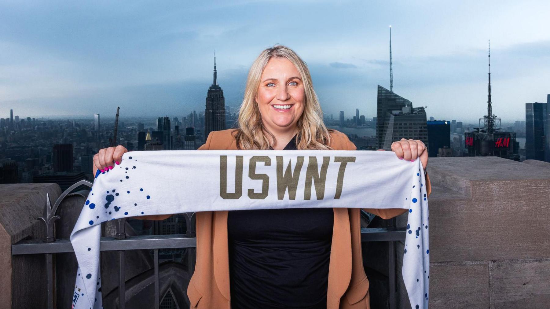 Emma Hayes holds a USWNT scarf at the top of the Rockefeller Center