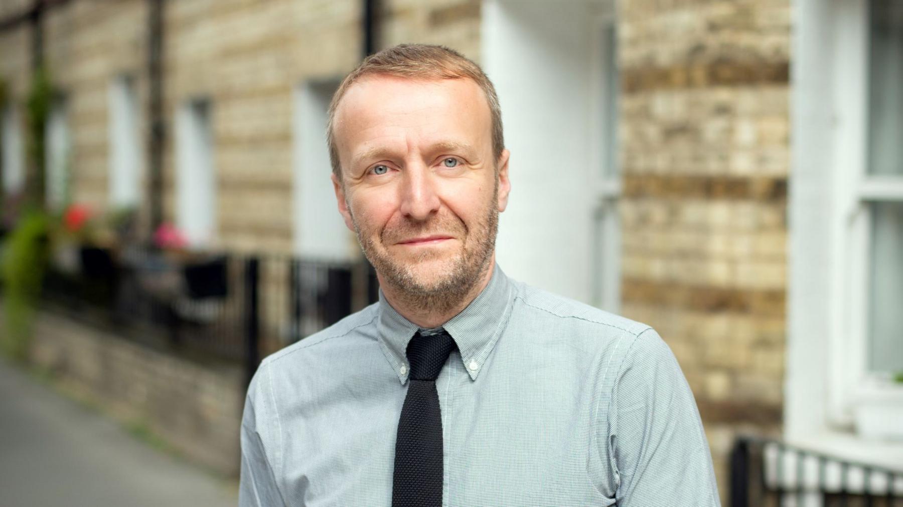 Ivan Mato wearing a tie and button-down collar looks into the camera.