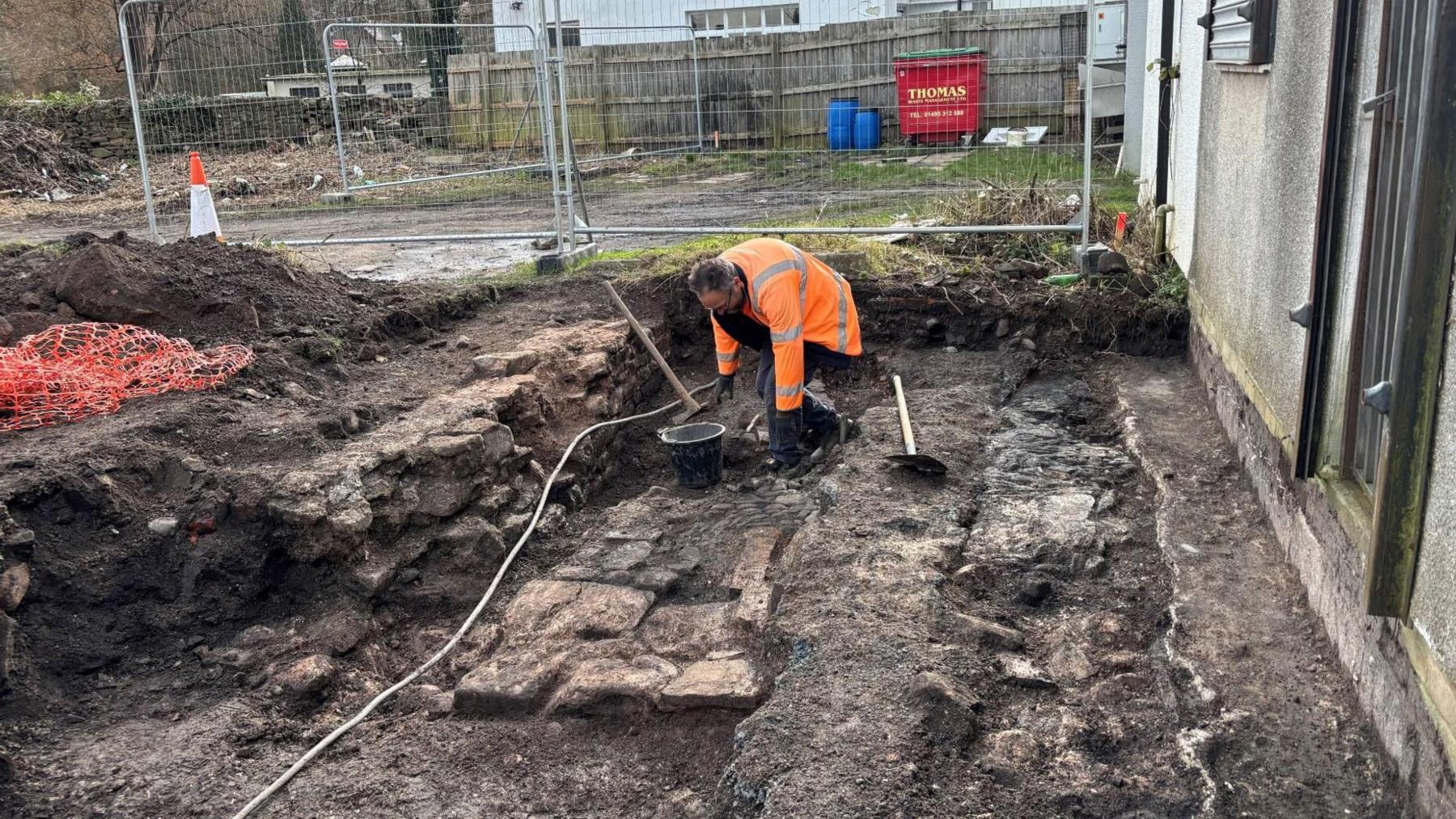 Llun o weithiwr yn cloddio. Gellir gweld olion hen waliau o hen adeilad Plas Gunter