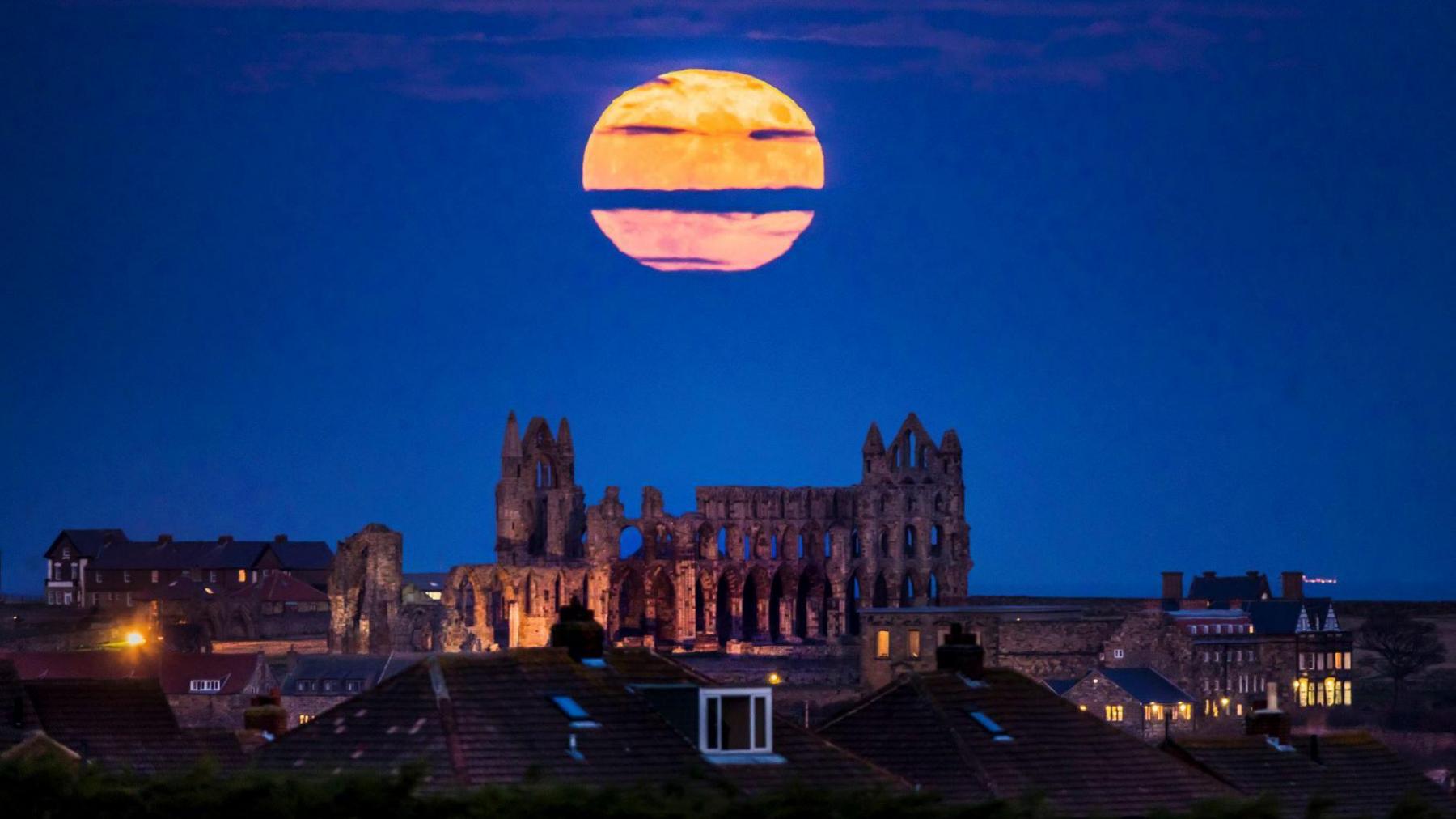 The bright, large supermoon is is in the night sky above Whitby Abbey