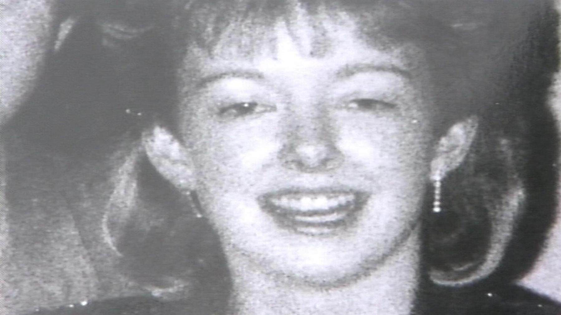 A black and white photograph of Diane Sindall, who has her hair cut into a fringe, smiling at the camera