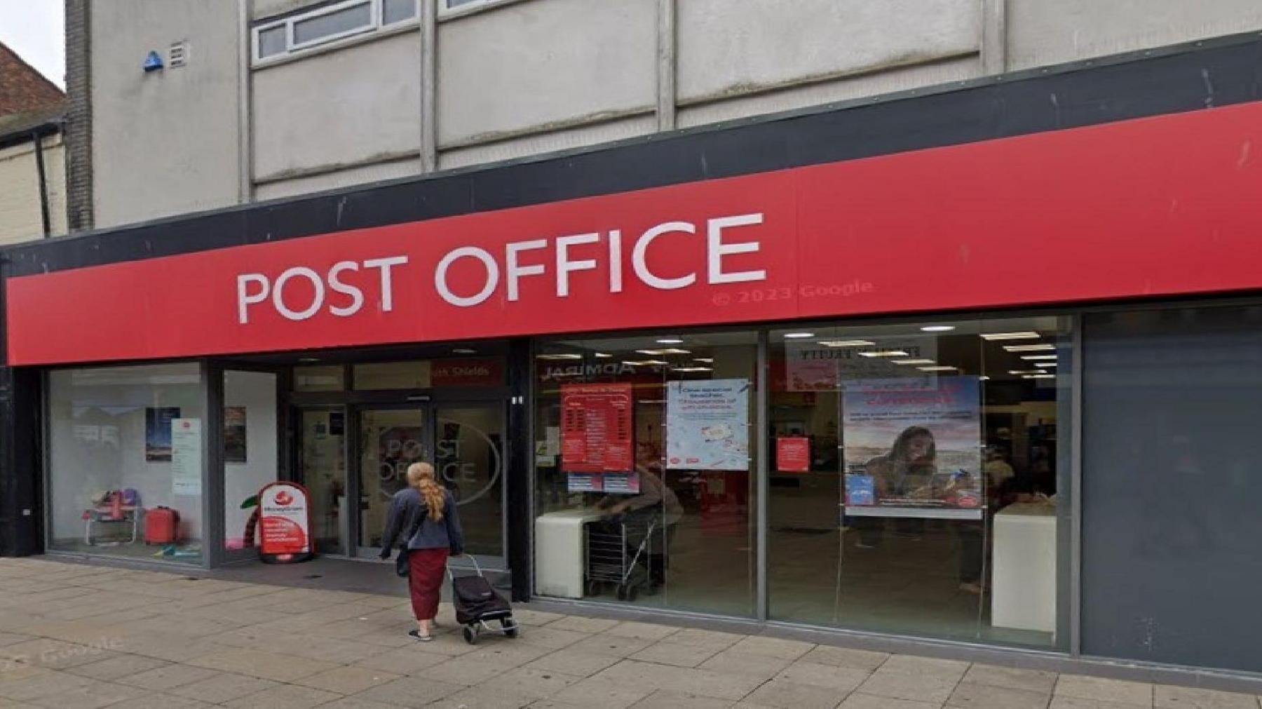 Frontage of a post office branch in South Shields. There is white lettering reading 'POST OFFICE' against a red fascia. A woman with a trolley is walking towards the front door.