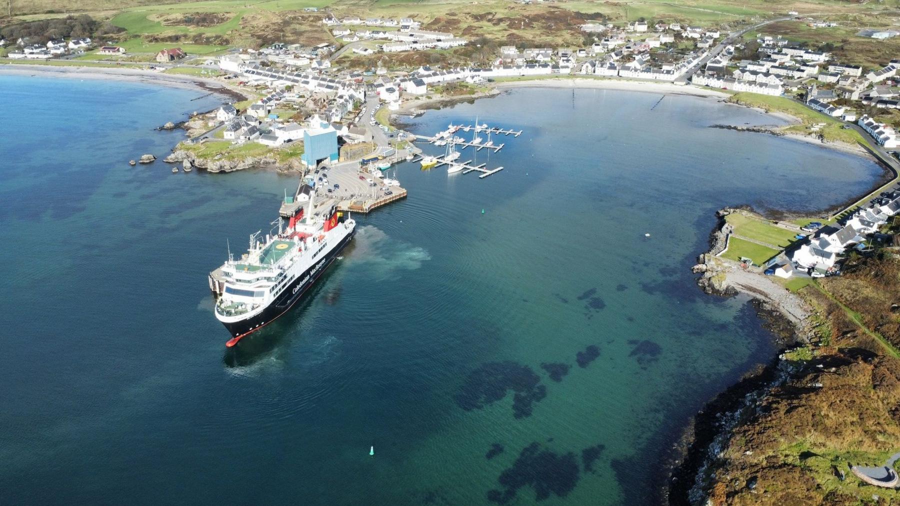 A curved bay with a pier at one end and a large black and white ferry beside it