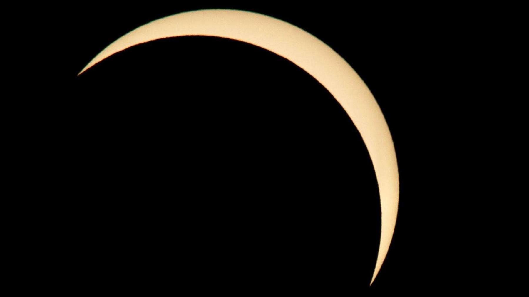 A semi-circled view of the sun, which is an off-white colour, in an otherwise black sky.