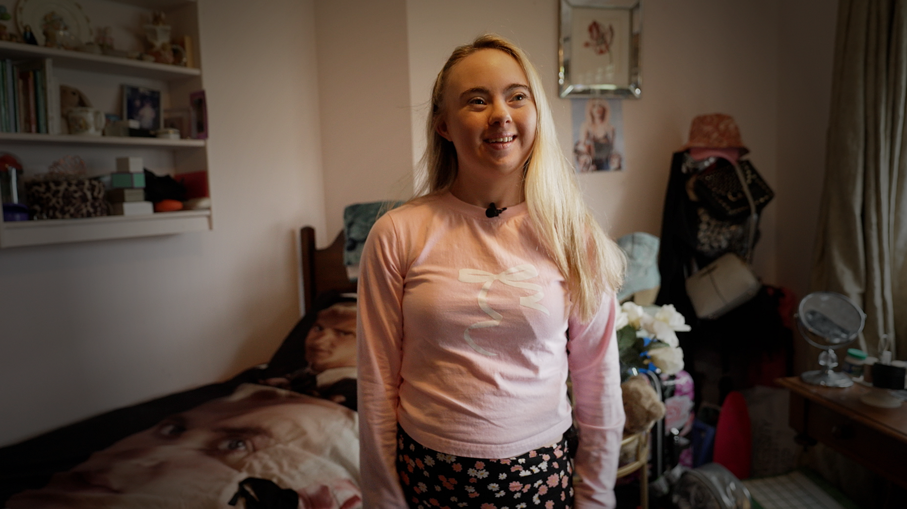 A young woman with Down's syndrome stands in her bedroom