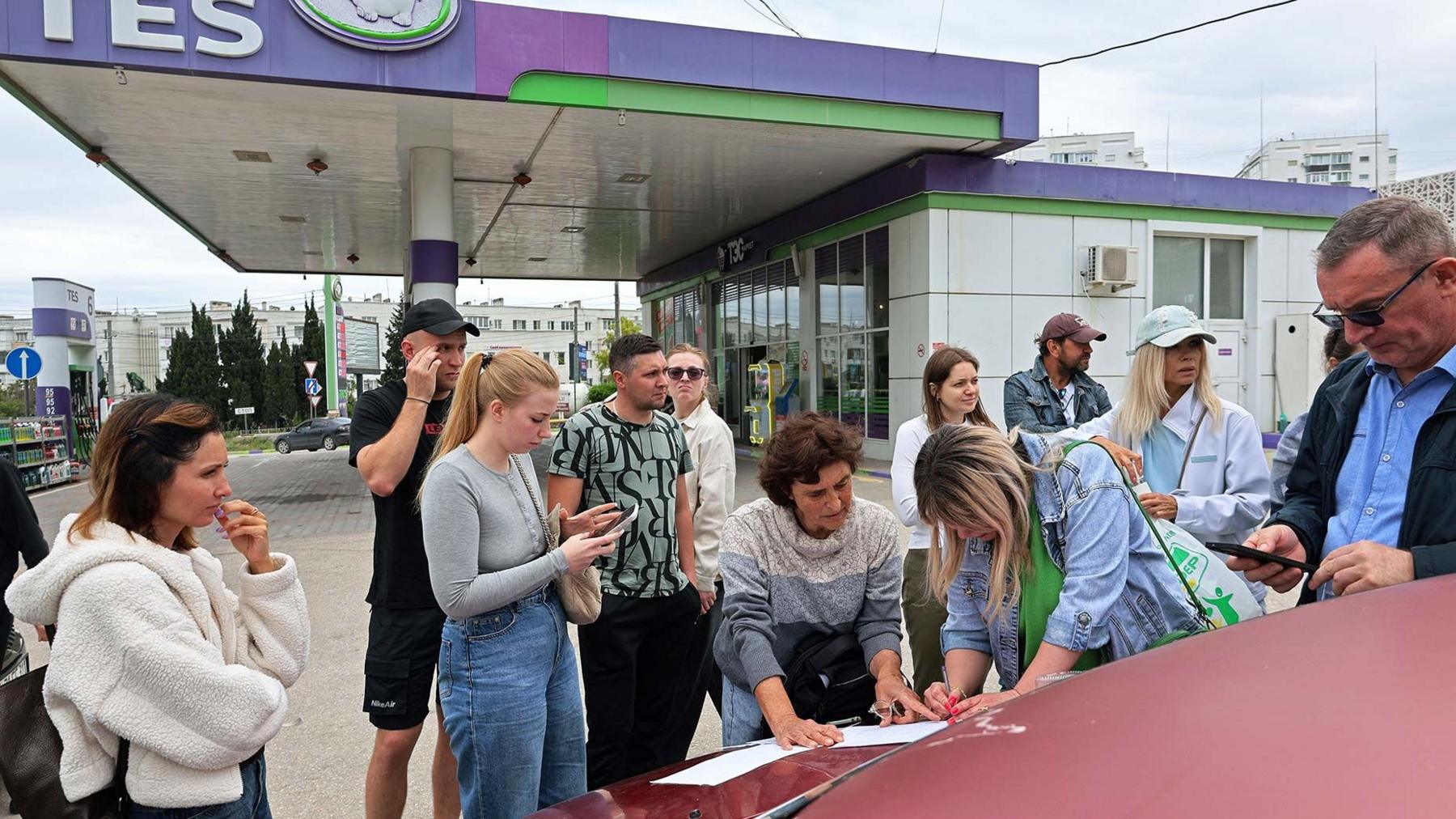 People dressed in casual clothing at a petrol station in Sevastopol, Crimea  leaning on a car bonnet putting their names on a list to join the queue for fuel after the authorities restricted fuel sales amid a supply shortage following Ukrainian attacks on logistics routes in the course of Russia-Ukraine conflict, June 1, 2026. 