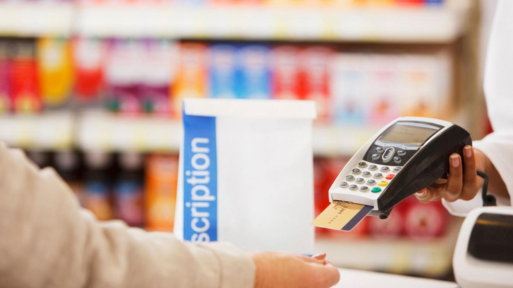 A generic getty image of someone paying for a prescription in a white bag at a pharmacy with medicines on shelves blurred in the background 