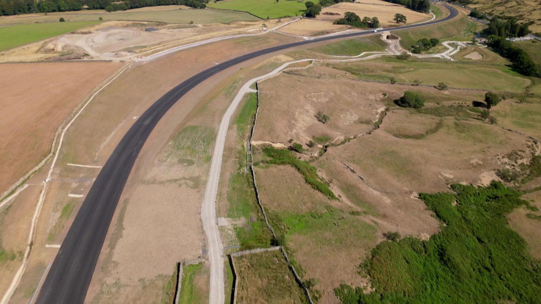 An aerial view of the new Kex Gill bypass, a tarmacked road running through a predominantly rural area with fields and moorland on either side.
