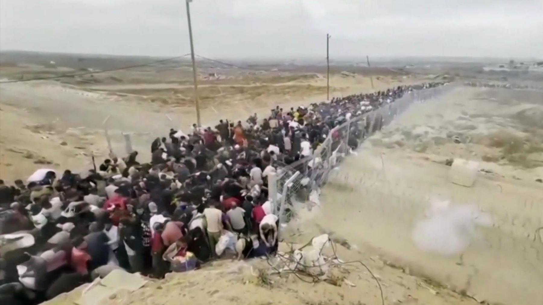 a congested queue of people in a fenced in corridor near a GHF site in Gaza