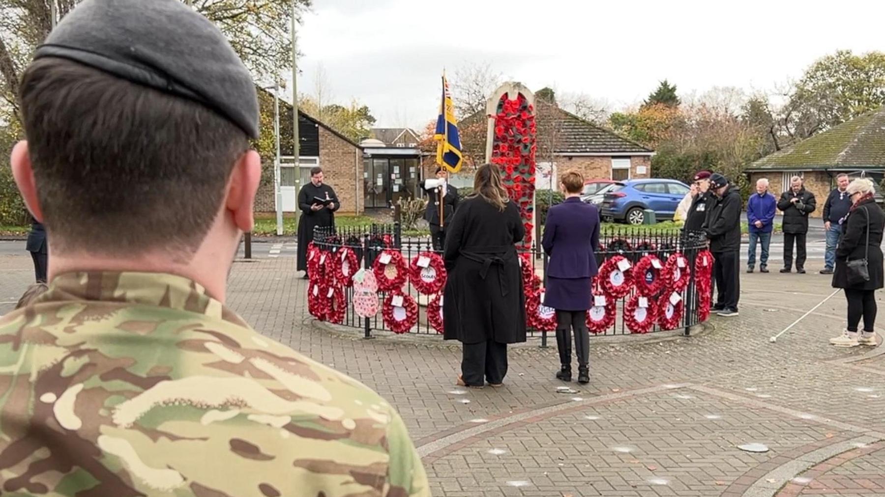 The back of a soldier dressed in camouflage and others stand during the two-minute's silence around a war memorial with poppy wreaths attached to the railings 