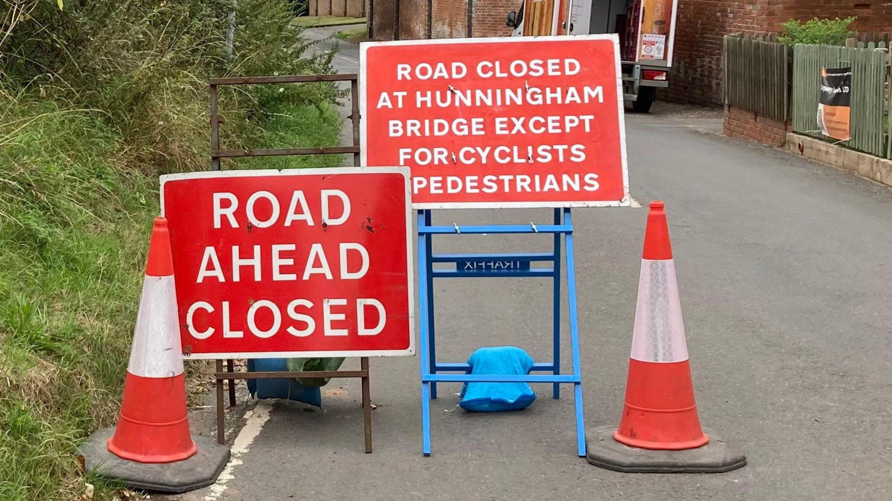 Two cones and red temporary road closure signs in the middle of the road.