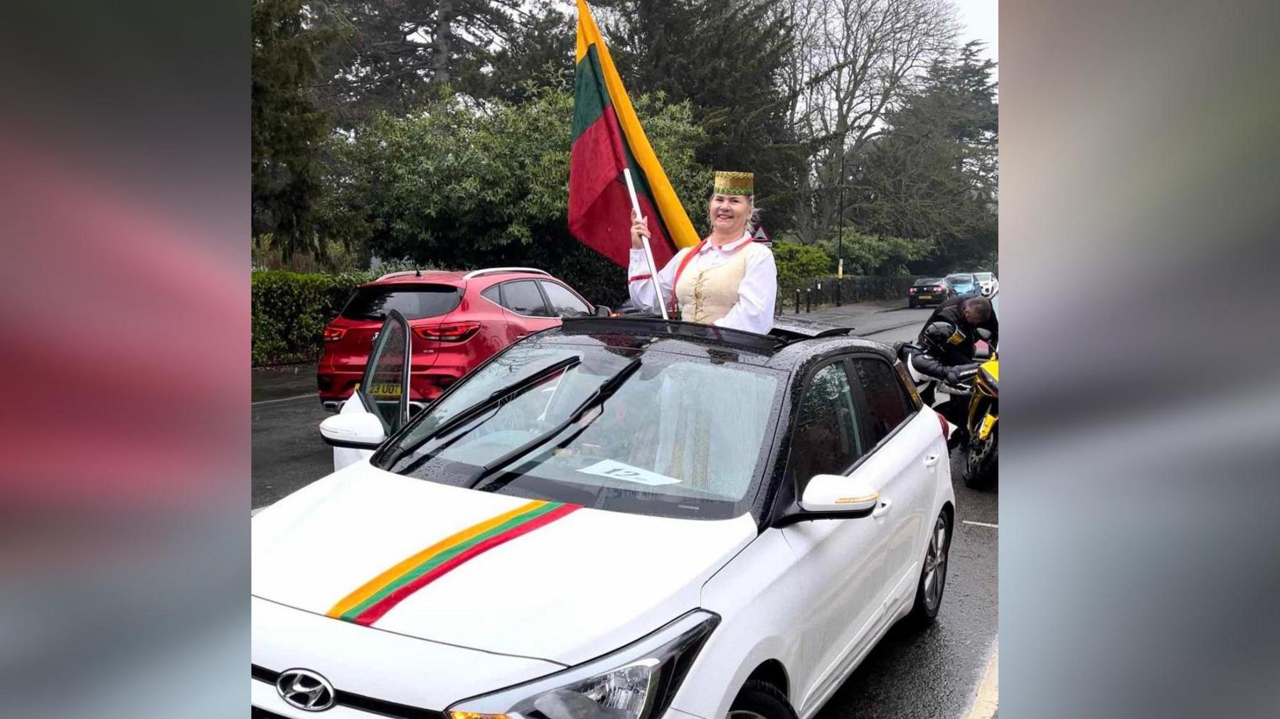 Lady dressed in traditional attire carrying a Lithuanian flag 