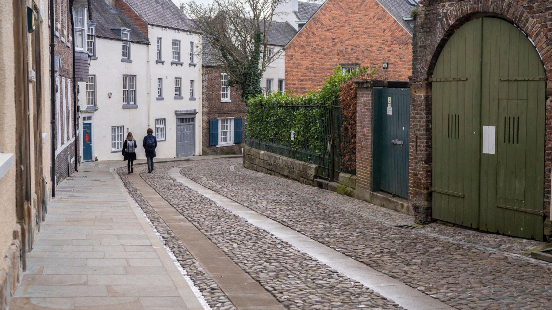 Cobbled street and two people walking along it in the background. 