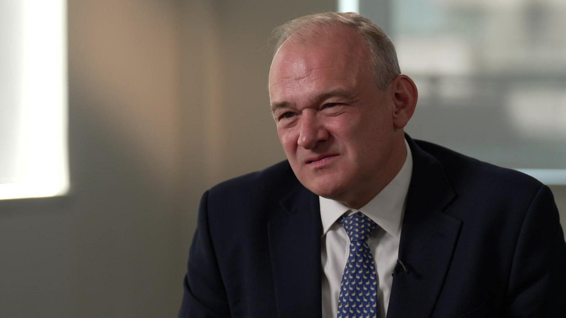 Ed Davey wears a dark suit, white shirt and a blue and white spotted tie.