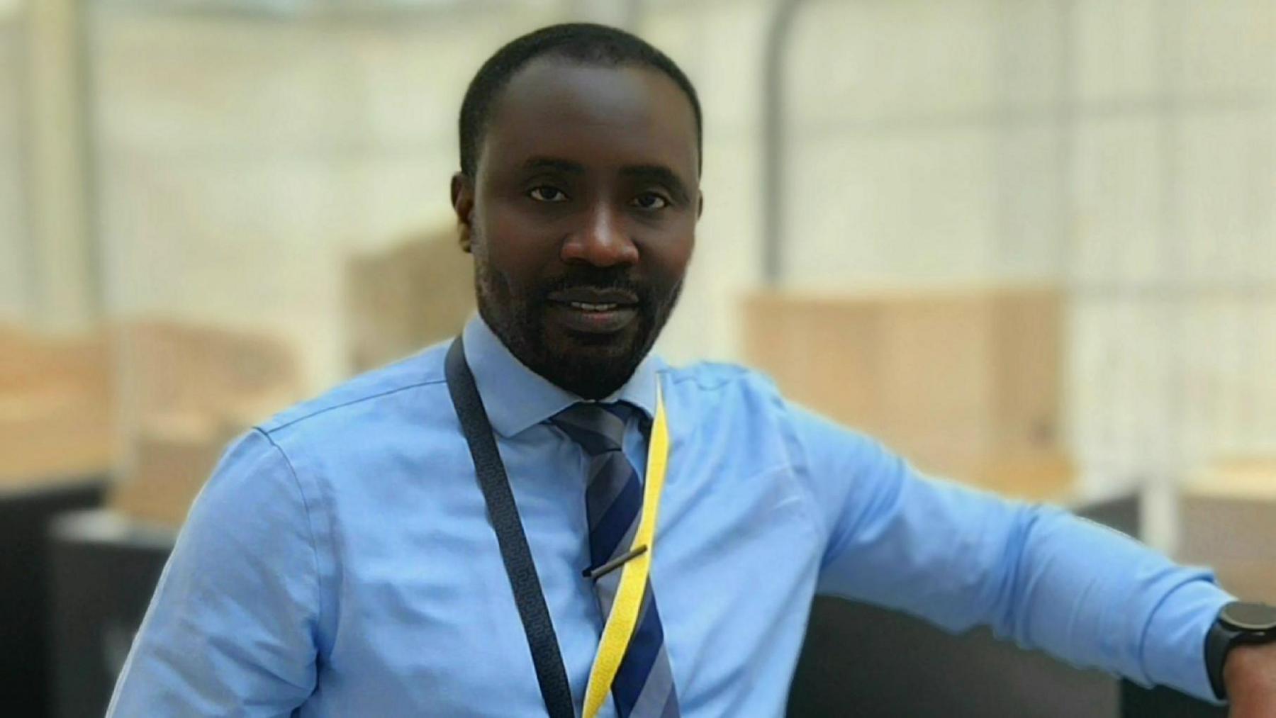 Titi looking at the camera, wearing a smart blue shirt, a striped tie and trousers.