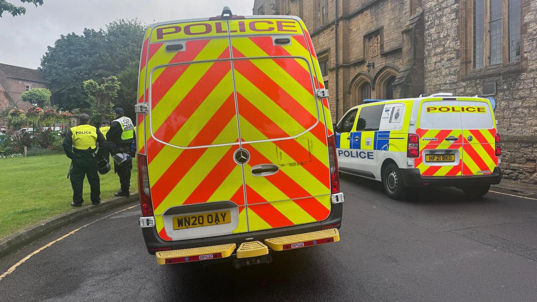 Two police vans outside a church, with two police officers stood next to one