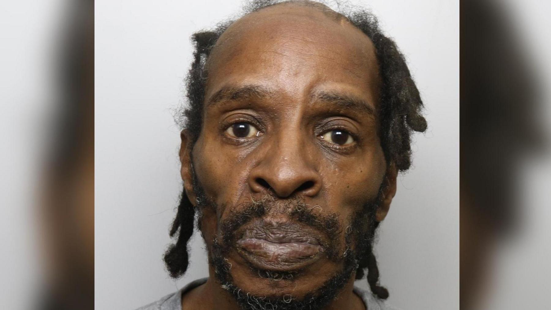 A custody picture of a man with black dreadlocks and a beard looking straight ahead at the camera. 